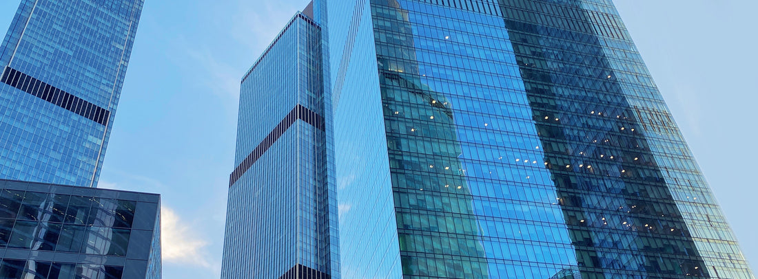 Low-angle shot of modern skyscrapers with blue and green glass facades reflecting the sky.