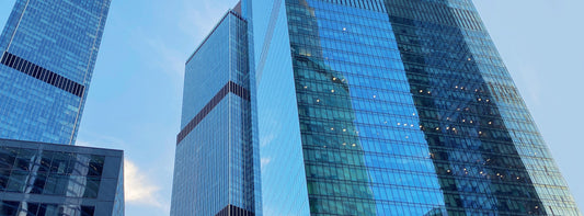 Low-angle shot of modern skyscrapers with blue and green glass facades reflecting the sky.